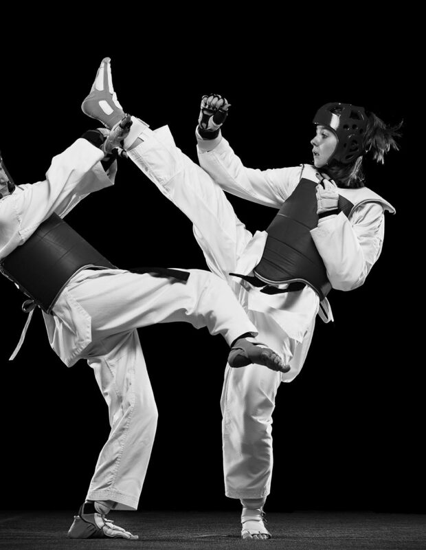 Full-length studio shot of two women, taekwondo athletes training isolated over black background