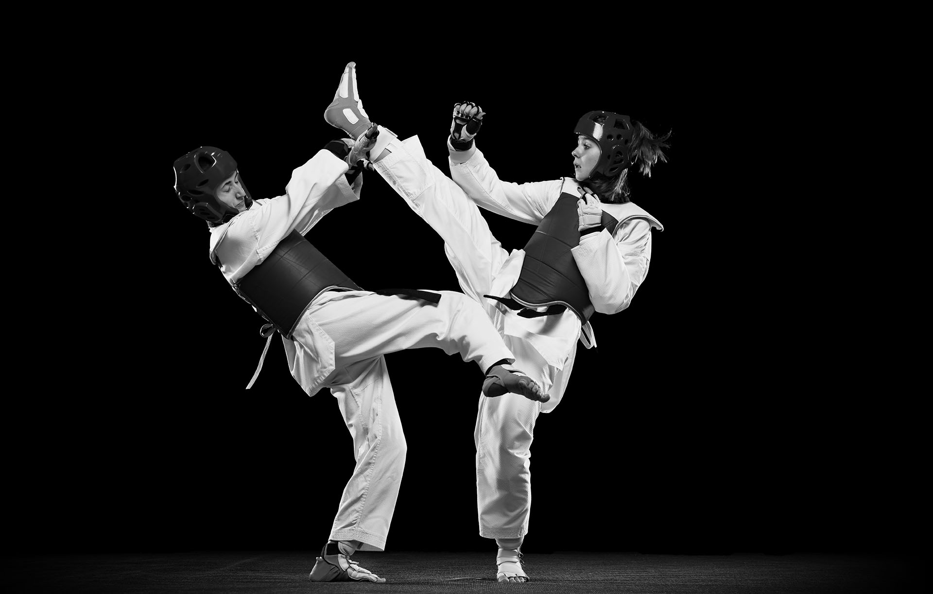 Full-length studio shot of two women, taekwondo athletes training isolated over black background